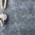 Silver whistle hanging on cord in front of chalkboard