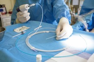 Person in scrubs and gloves holding medical device on draped table