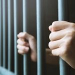Hands grasping around prison bars